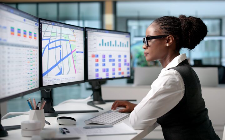 A delivery coordinator at a desk, tracking orders across three screens
