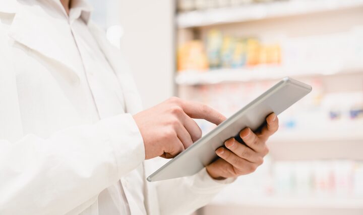 A pharmacist using a tablet in front of the dispensary shelves