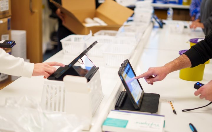 A driver and a pharmacy team member confirming a delivery on rugged tablets, scanning each item as it is signed for