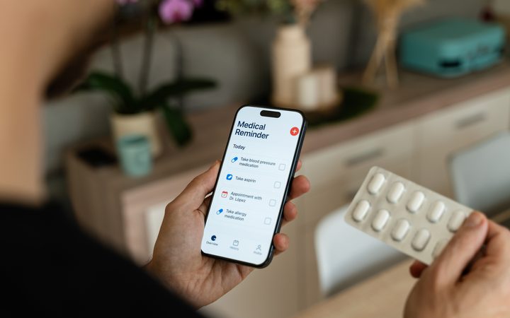 A medication reminder app on a phone, held beside a blister pack of tablets