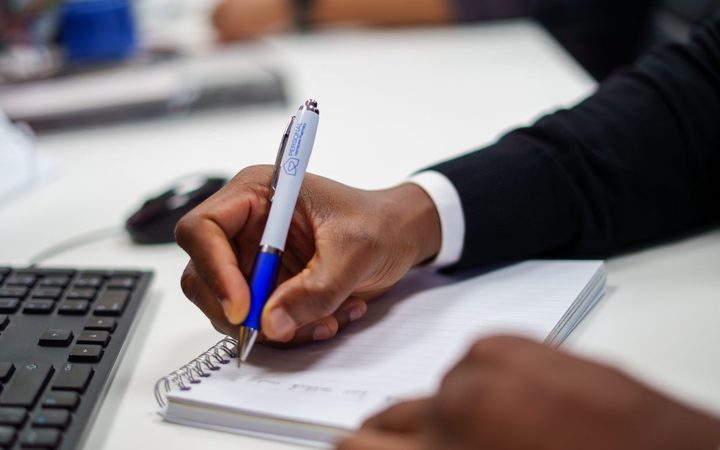 A team member writing notes in a pad with a Personal Homecare Pharmacy branded pen