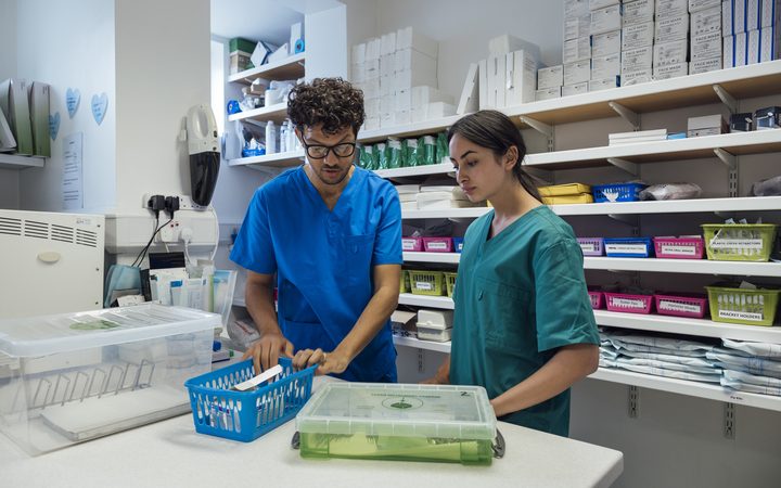 Two pharmacy team members in scrubs sorting medicines into baskets in a dispensary