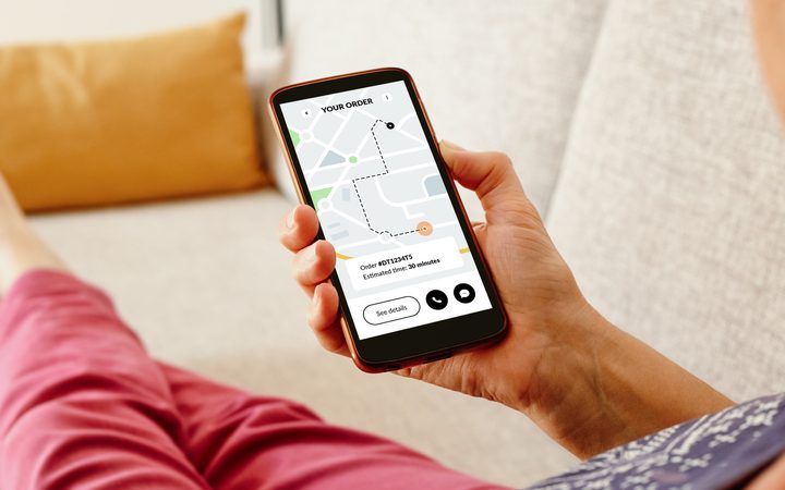 A patient on a sofa following a delivery's route on a phone