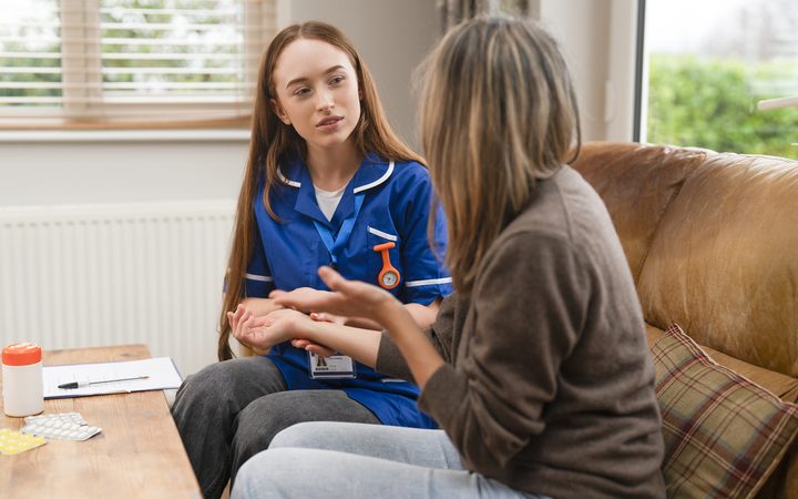 A nurse in uniform sitting with a patient in her living room