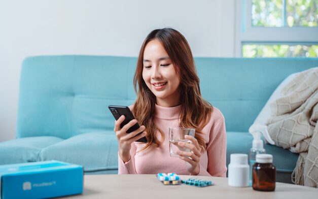 A patient at home on her sofa checking her phone, with her medication on the table